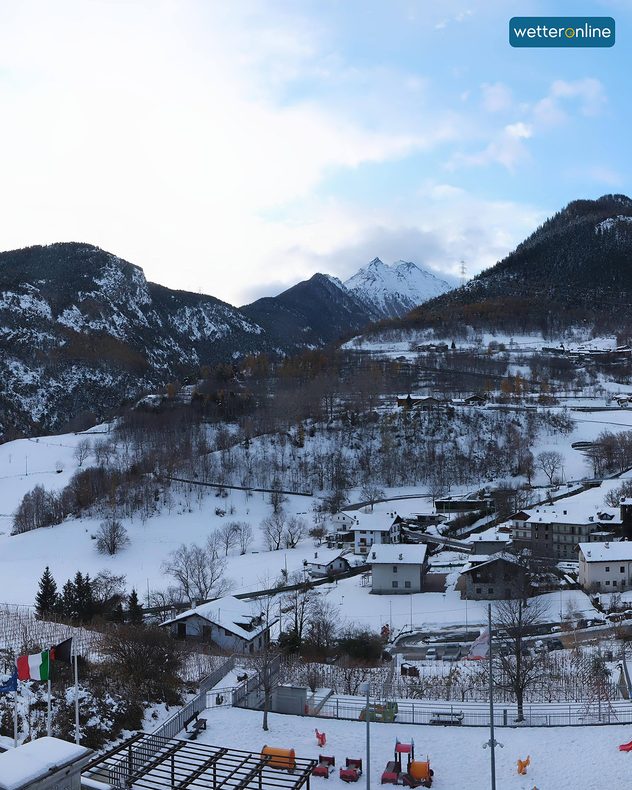 Village alpin enneigé entouré de montagnes et d'un ciel hivernal clair. Aire de jeux et drapeaux au premier plan.
