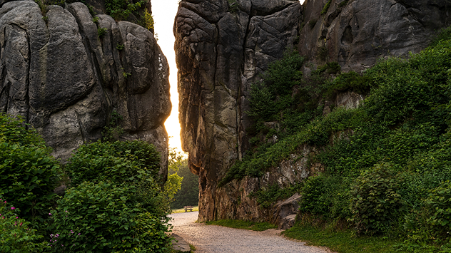Sonnenuntergang zwischen den Externsteinen im Teutoburger Wald bei Horn-Bad Meinberg, flankiert von steilen Felswänden und grüner Vegetation.