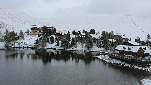 © foto-webcam.eu Das Bild zeigt eine verschneite Berglandschaft mit einem See im Vordergrund – offenbar in den Alpen. Mehrere Hütten liegen am Ufer, und die Hänge sind frisch mit Schnee bedeckt