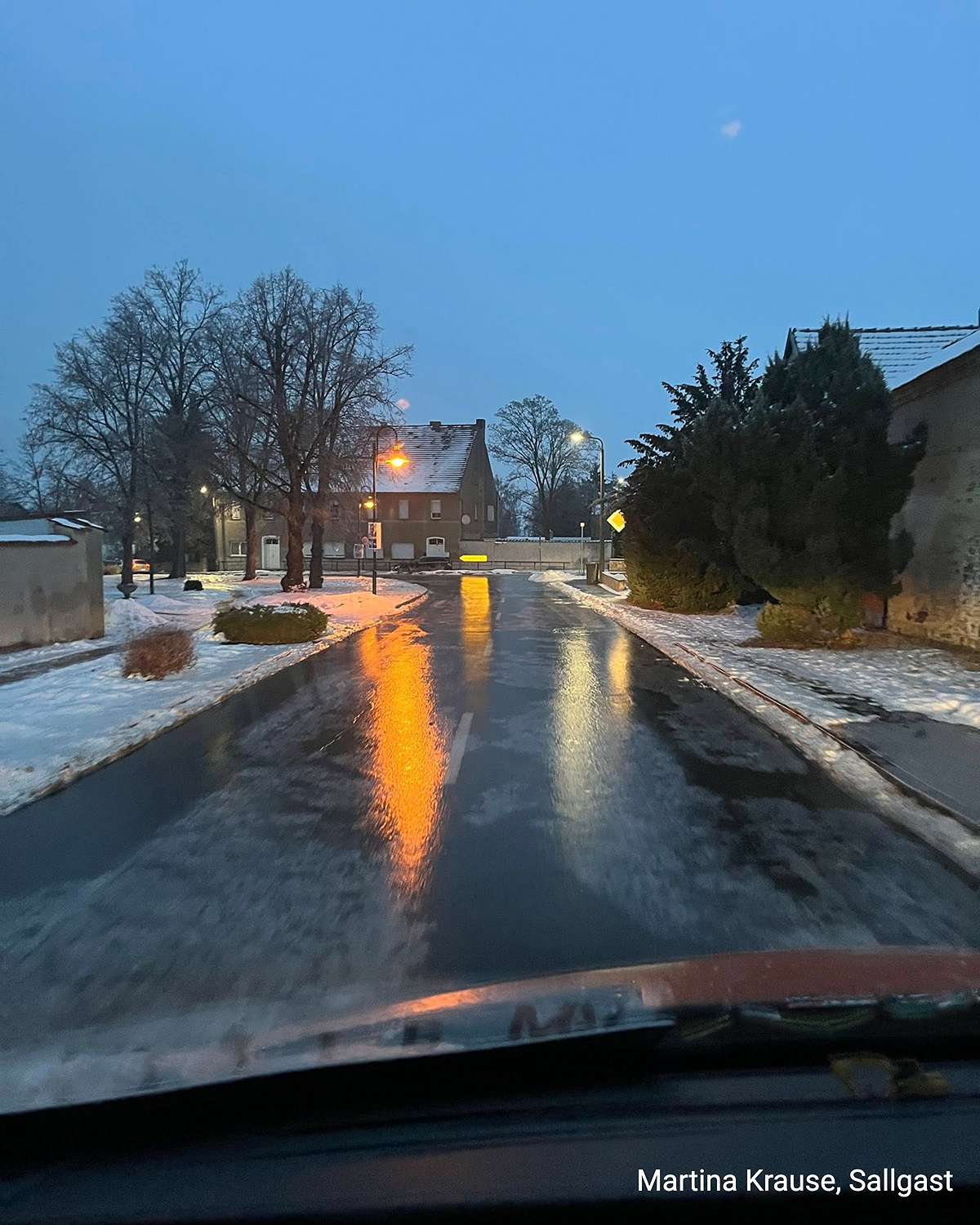 Nasse, vereiste Straße bei Dämmerung, Lichtspiegelungen auf Eisfläche in Sallgast.