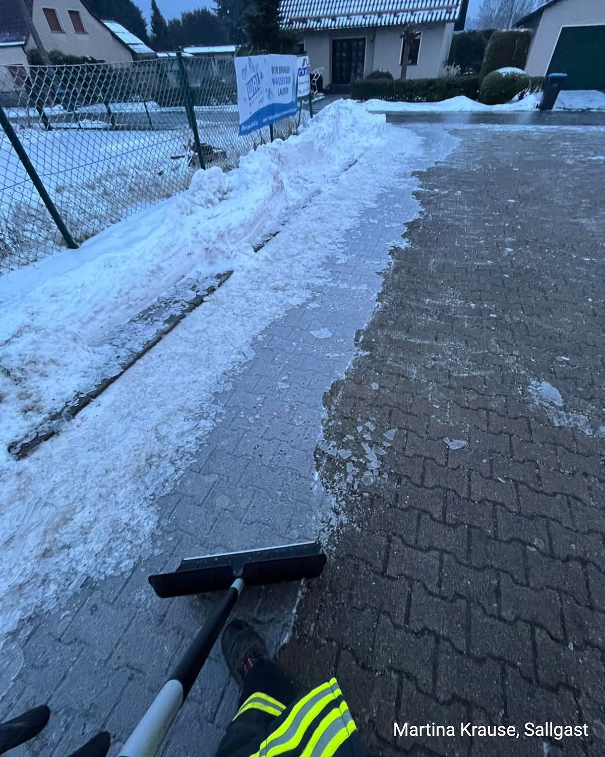 Gehweg mit Eisschicht, eine Person entfernt Eis mit einem Schieber in Sallgast.