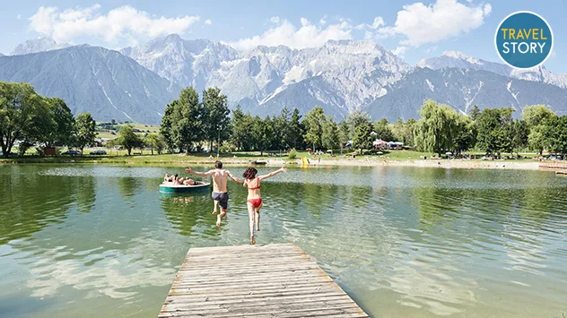 Ein Paar springt von einem Steg in den Mieminger See, im Hintergrund Bergkulisse.