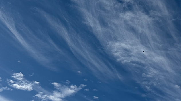 High wispy cirrus clouds streaking across a deep blue sky, with a small distant aircraft visible near the upper right.