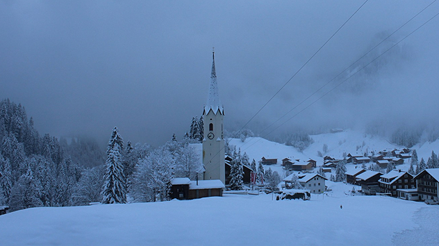 Besneeuwde kerk in mistig winterlandschap met huizen en bomen. Rustig landschap in dikke verse sneeuw.