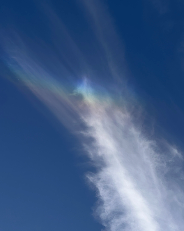 Wispy white cloud shows faint green, blue, and pink iridescent colours against a deep blue sky.