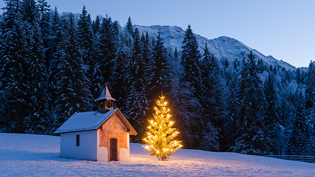 Eine kleine Kapelle und ein beleuchteter Weihnachtsbaum stehen auf einer schneebedeckten Wiese