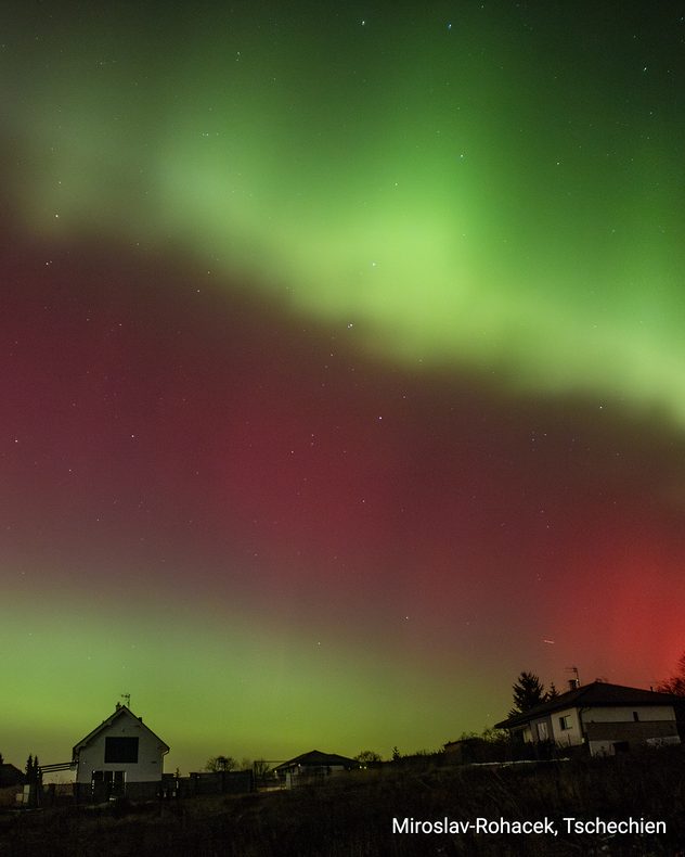 Grün-rotes Polarlicht über Häusern bei Nacht. Wohngebiet in Tschechien.