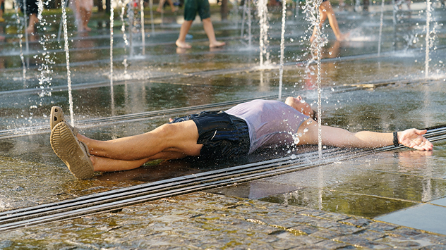 Mann liegt zwischen einem Springbrunnen auf dem Boden und kühlt sich ab.