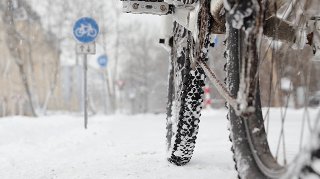 Fahrradreifen auf verschneitem Radweg, Schnee und Eis haften am Profil, winterliche Straßenverhältnisse.