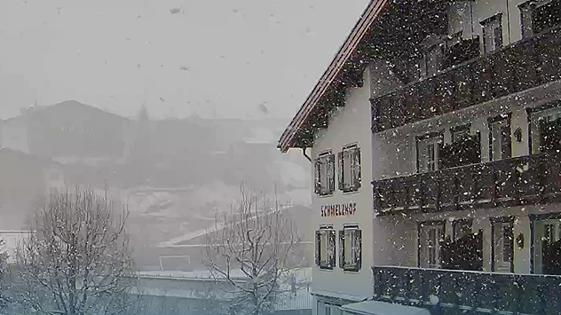 Dichter Schneefall über Lech am Arlberg. Im Vordergrund steht ein verschneites Hotelgebäude, dahinter sind Berge und Häuser im Nebel erkennbar.