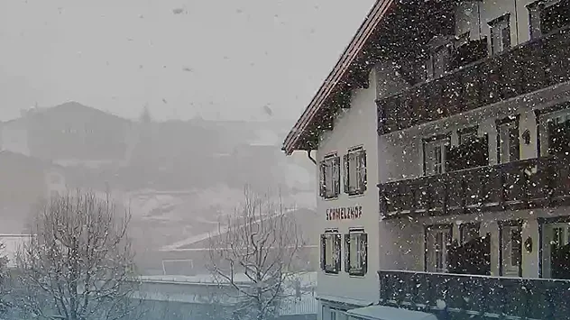 Dichter Schneefall über Lech am Arlberg. Im Vordergrund steht ein verschneites Hotelgebäude, dahinter sind Berge und Häuser im Nebel erkennbar.