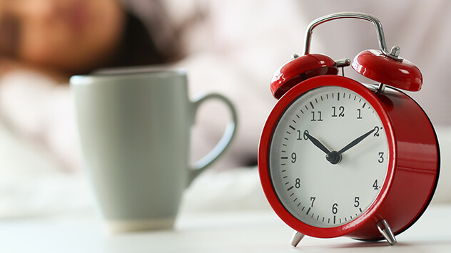 Schlafende Frau mit rotem Wecker am Bett