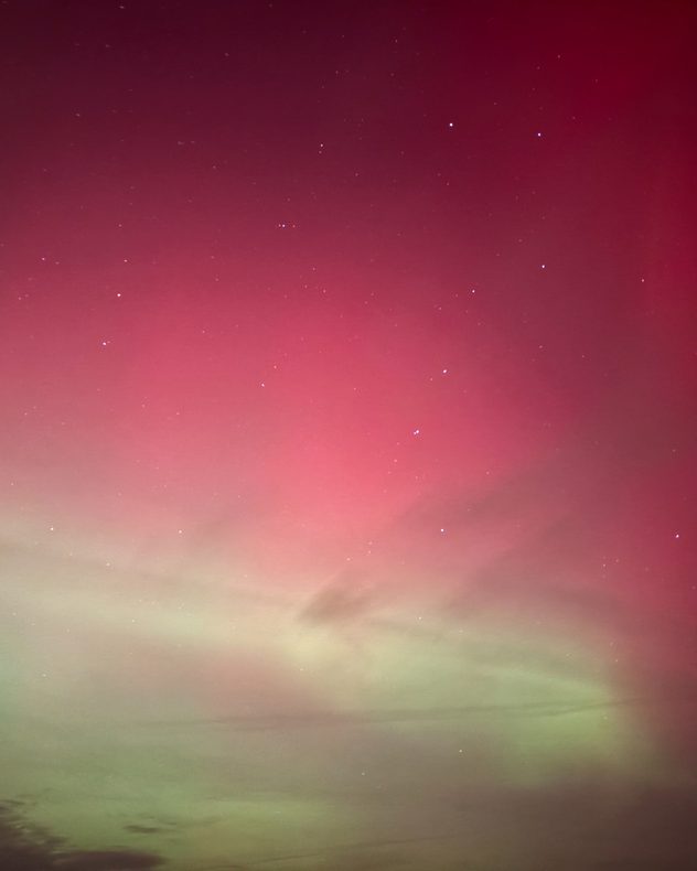 Night sky filled with deep red aurora glow fading into pale green near the horizon, with scattered stars visible through thin cloud layers.