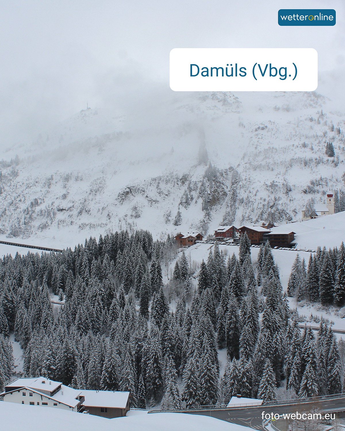 Das Webcambild zeigt eine verschneite Berglandschaft mit einer Passstraße und ein paar Häusern.