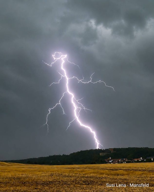 Heller, verzweigter Blitz vor dunklem Gewitterhimmel über einem Feld bei Mansfeld.