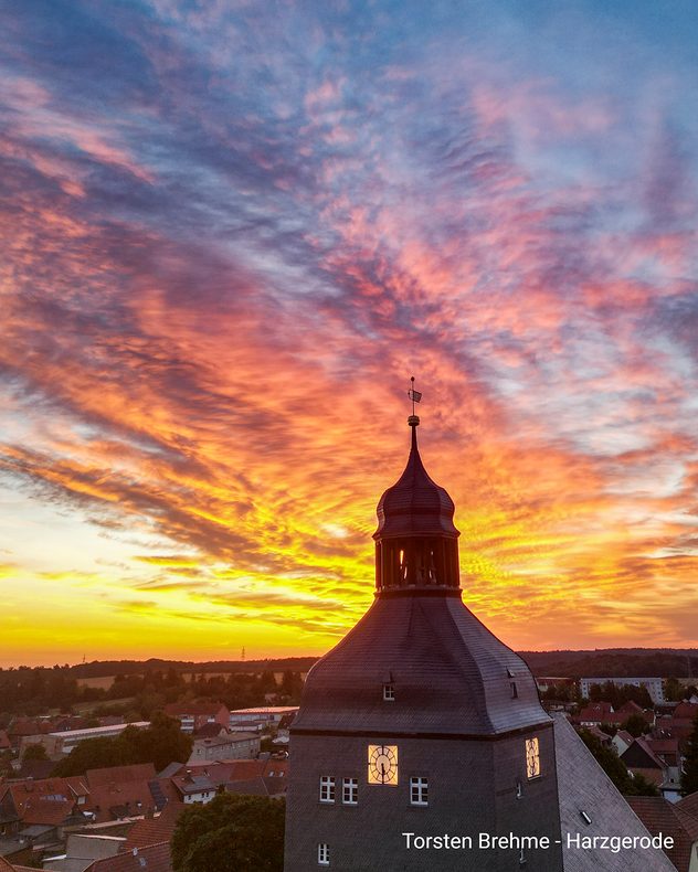 Kirchturm von Harzgerode vor einem farbenprächtigen Abendhimmel mit orange und rosa leuchtenden Wolken.