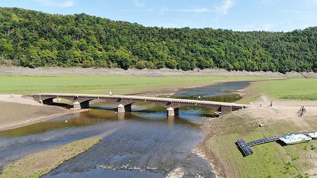 Trockengefallene Aseler Brücke am Edersee mit nur noch wenig Wasser, umgeben von trockenen Flächen und Spaziergängern. (c) dpa