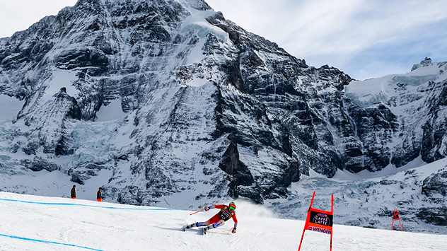 Das Bild zeigt einen Skirennfahrer auf der Lauberhornabfahrt. Im Hintergrund sind der Mönch und das Jungfraujoch zu sehen.