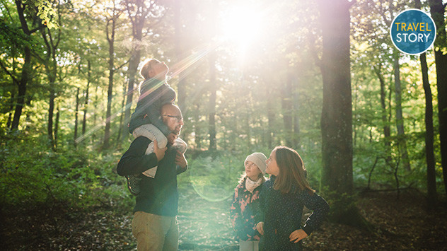 Ein Vater mit drei Kindern im Wald, die Sonne scheint durch die Baumwipfel.