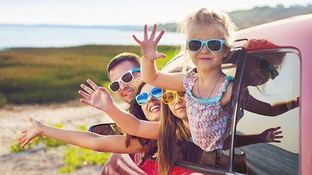 Eine Familie, die vor einer Reise zum Abschied aus dem Auto winkt