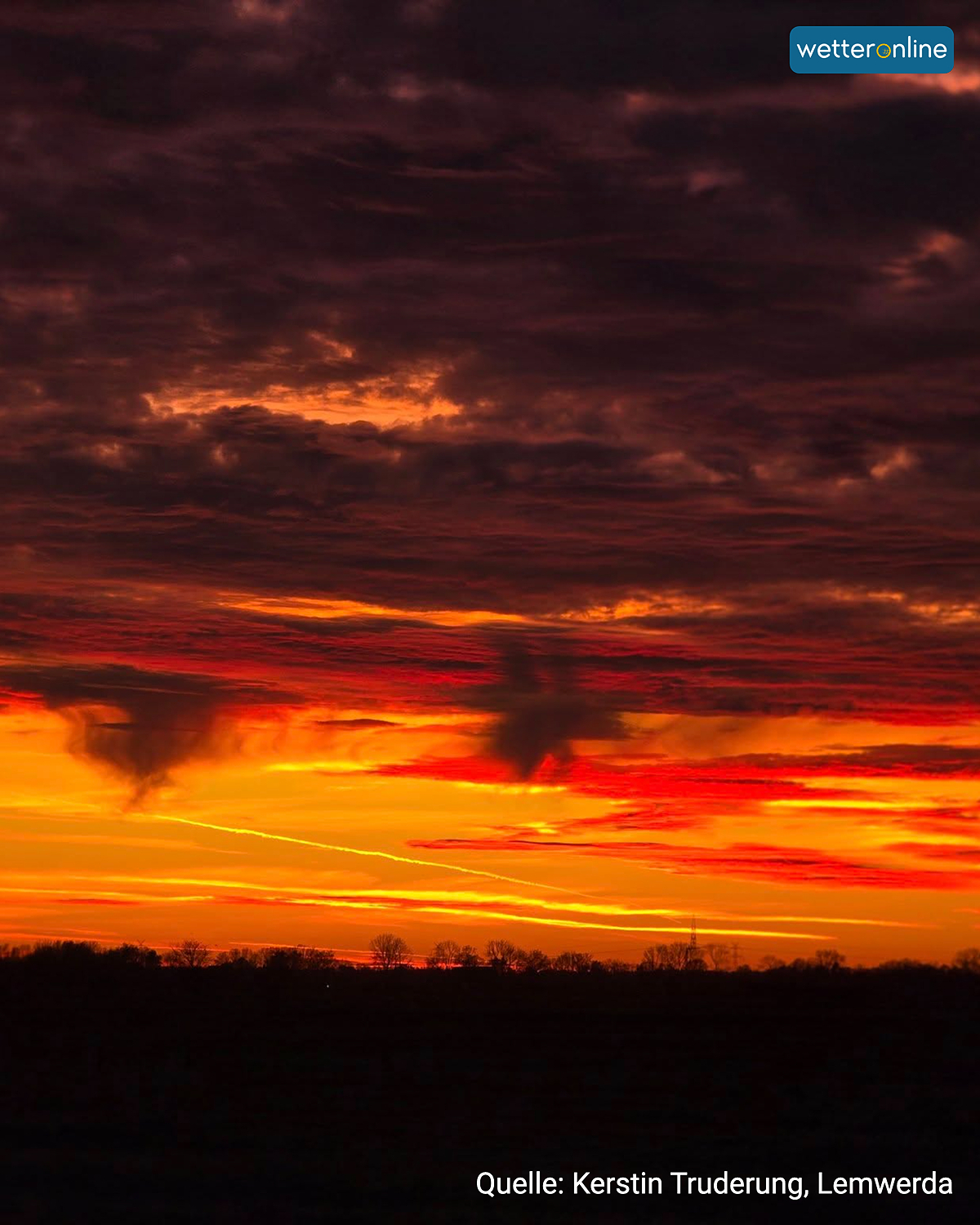 Leuchtend roter Sonnenuntergang unter dunklen Wolken über flacher Landschaft.