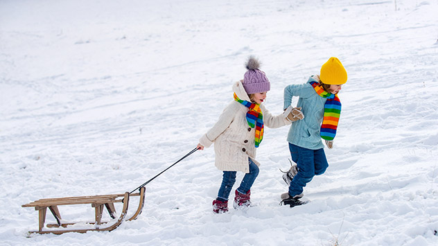 Zwei Kinder ziehen einen Schlitten über eine schneebedeckte Wiese
