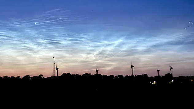 Leuchtende Nachtwolken über Fehmarn mit Windrädern als Silhouetten am Horizont.
