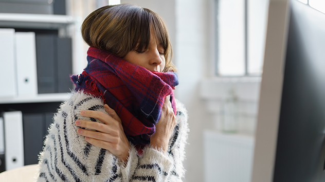 Eine junge Frau sitzt am Schreibtisch und friert. 