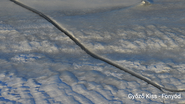 Detailaufnahme der Eisoberfläche auf dem Plattensee. Ein dunkler Riss zieht sich durch das gefrorene Eis. Die Oberfläche zeigt raue, gefrorene Strukturen.
