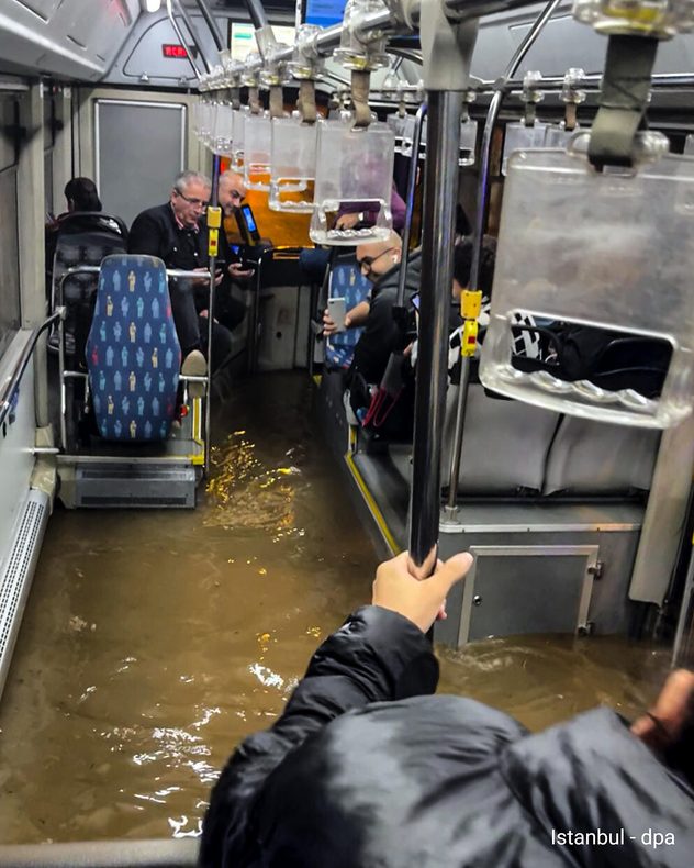 Er staat bruin hoogwater in het interieur van een bus in Istanbul. Verschillende passagiers zitten op verhoogde zitplaatsen, terwijl het gangpad onder water staat.