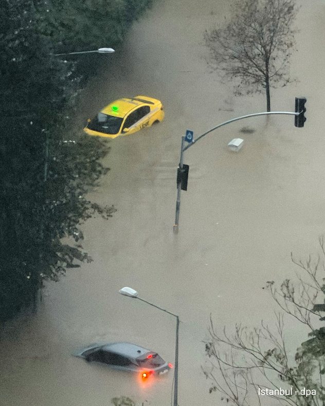 Een ondergelopen straat in Istanbul. Een gele taxi en nog een auto staan diep in het bruine hoogwater. Ook de verkeerslichtmasten steken uit het water.