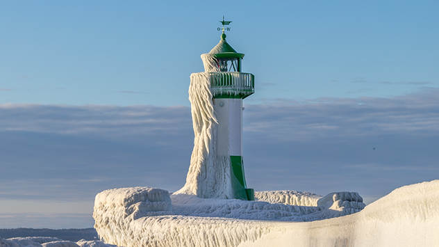 Eis und Wind haben den Leuchtturm erstarren lassen. Ein eindrucksvolles Beispiel extremer Winterkälte. Die Küste zeigt sich tiefgefroren.