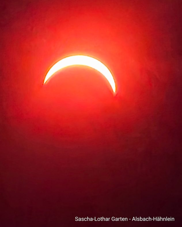 Partielle Sonnenfinsternis über Alsbach-Hähnlein. Vor rötlichem Hintergrund ist die Sonne als schmale, helle Sichel zu sehen.