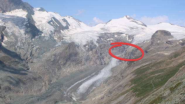 Blick auf einen stark zurückgegangenen Gletscher in einer hochalpinen Berglandschaft. Ein roter Kreis markiert einen felsigen Bereich oberhalb der Gletscherzunge.