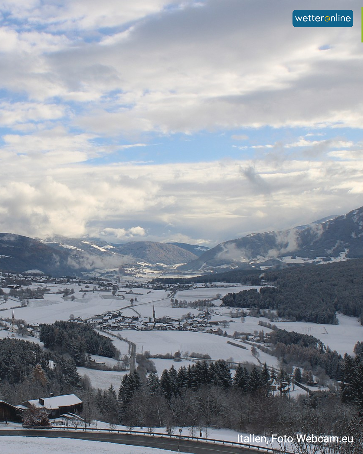 Verschneites Tal in Südtirol mit Dörfern und Bergen unter teils bewölktem Himmel.
