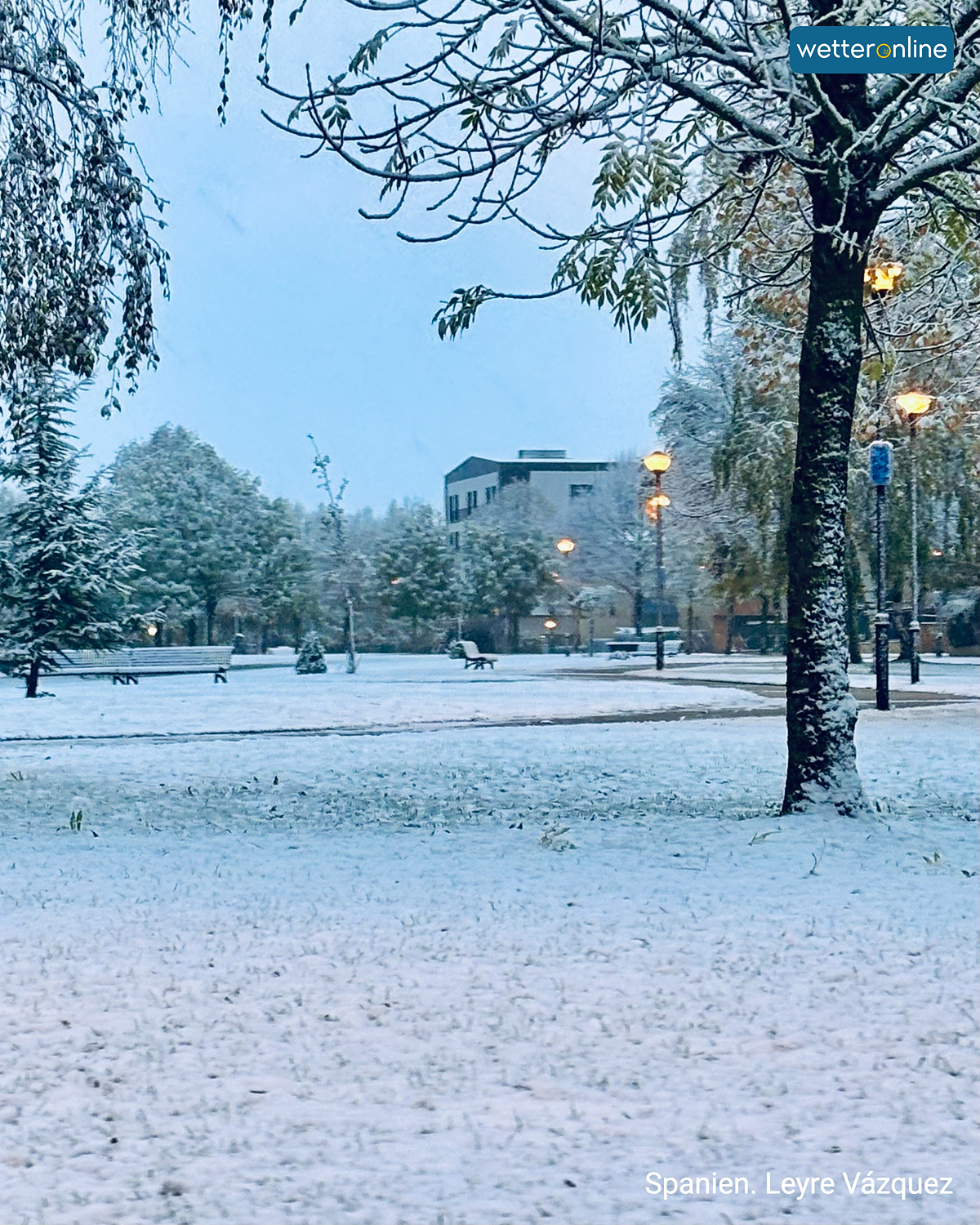 Verschneiter Park in Spanien mit beleuchteten Laternen am frühen Morgen.