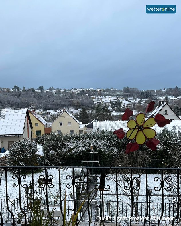 Blick von einem Balkon auf verschneite Gärten und Dächer in einem Wohngebiet.