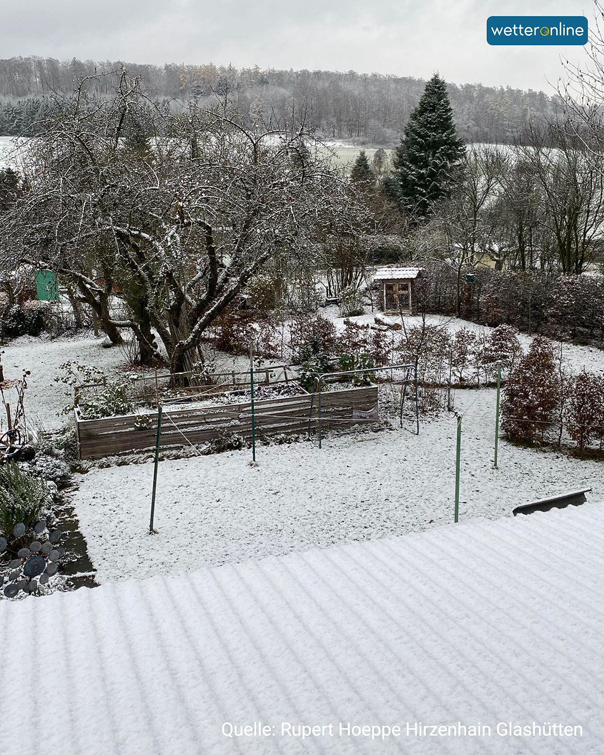 Garten mit Bäumen und Beeten, leicht mit Schnee bedeckt.