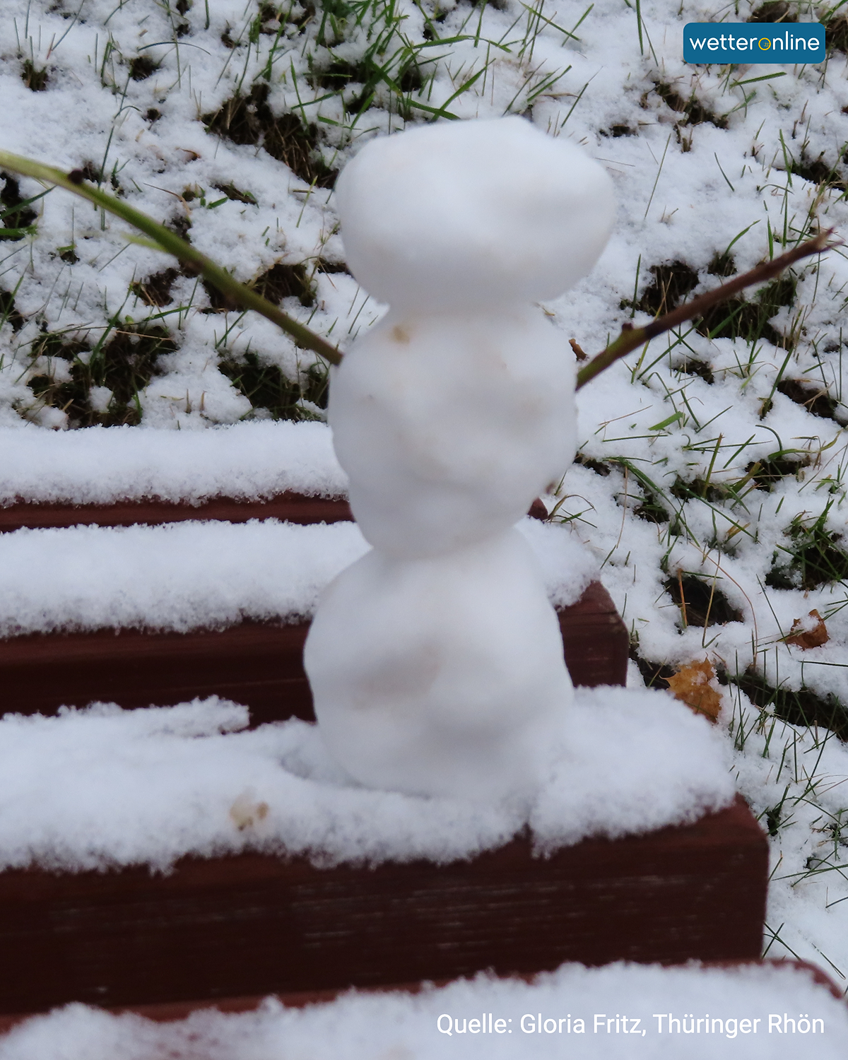 Kleiner Schneemann aus drei Schneekugeln auf einer Bank mit Schneeresten.