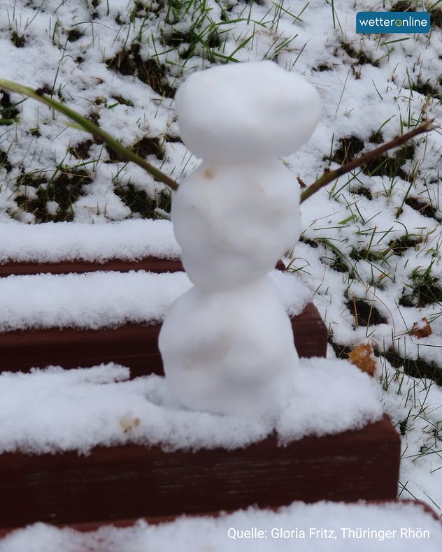 Kleiner Schneemann aus drei Schneekugeln auf einer Bank mit Schneeresten.