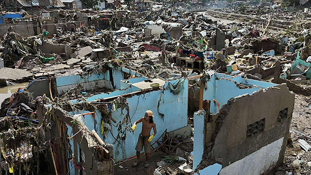 Man standing in the ruins of destroyed houses after a natural disaster.