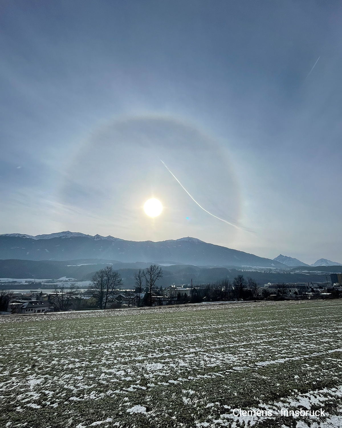 Nisko sunce nad zimskim krajolikom. Svijetli prsten tvori sunčev oreol na nebu. U pozadini se vide planine u blizini Innsbrucka.