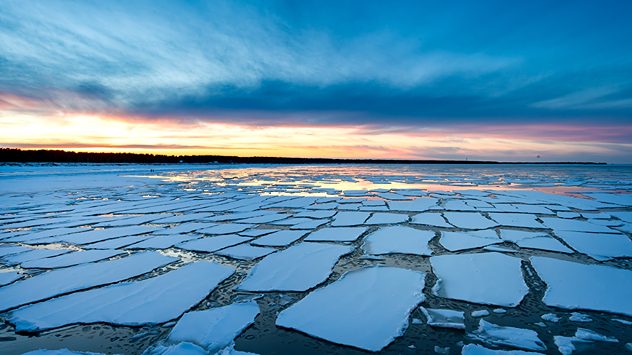 Aufgebrochene Eisschollen auf einem See bei Sonnenaufgang. Bunter Himmel über einer weiten Winterlandschaft. (c) Klaus Haase
