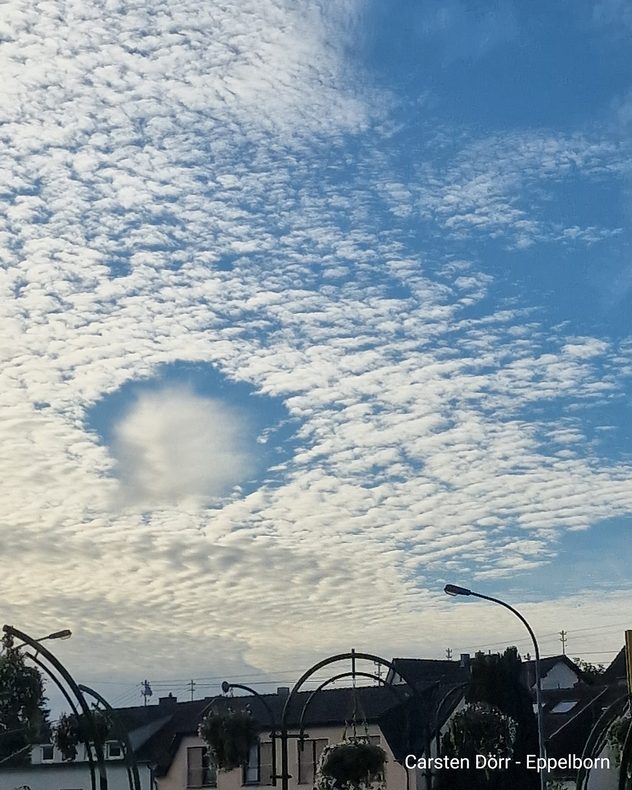 Rundes Wolkenloch in einer Schäfchenwolkendecke über Häusern in Eppelborn im Saarland.