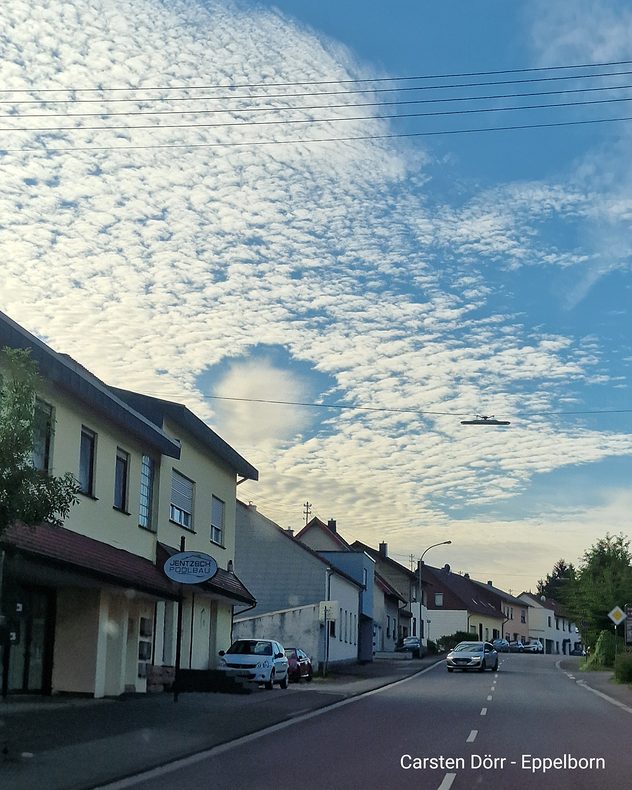 Rundes Wolkenloch in einer Schäfchenwolkendecke über einer Häuserzeile in Eppelborn im Saarland.