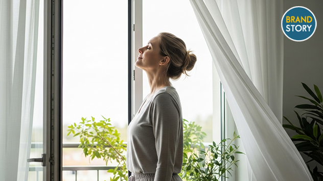 Eine Frau nimmt einem tiefen Atemzug am geöffneten Fenster.