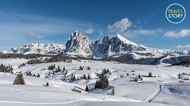 Verschneite Winterlandschaft auf der Seiser Alm mit Blick auf die markanten Dolomiten-Gipfel unter blauem Himmel.