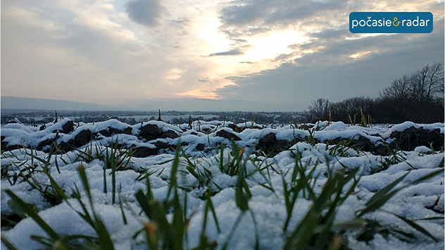 Zvyšky snehu na tráve pri západe slnka, zamračená obloha nad krajinou