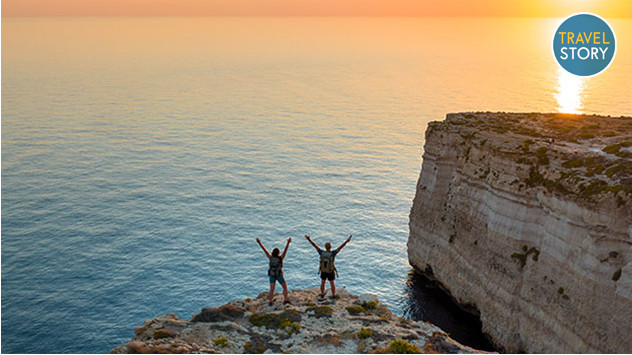 Zwei Wanderer auf einem Felsen blicken bei Sonnenuntergang aufs Meer.