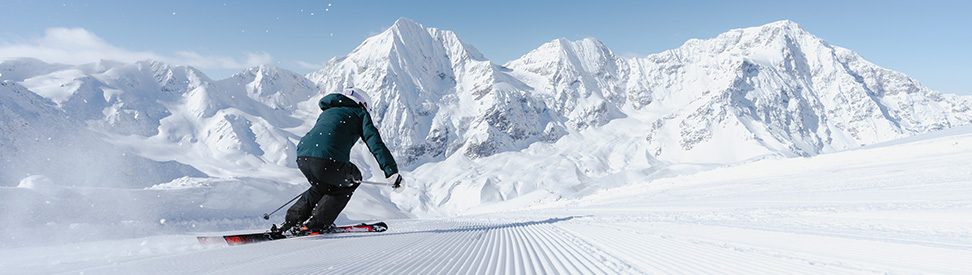 Ein Skifahrer fährt auf einer frisch präparierten Piste, im Hintergrund schneebedeckte Berge. (c) IDM SÃ¼dtirol / Thomas Monsorno